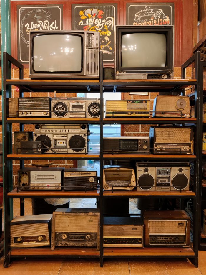 A collection of vintage radios and televisions displayed on metal shelves indoors.