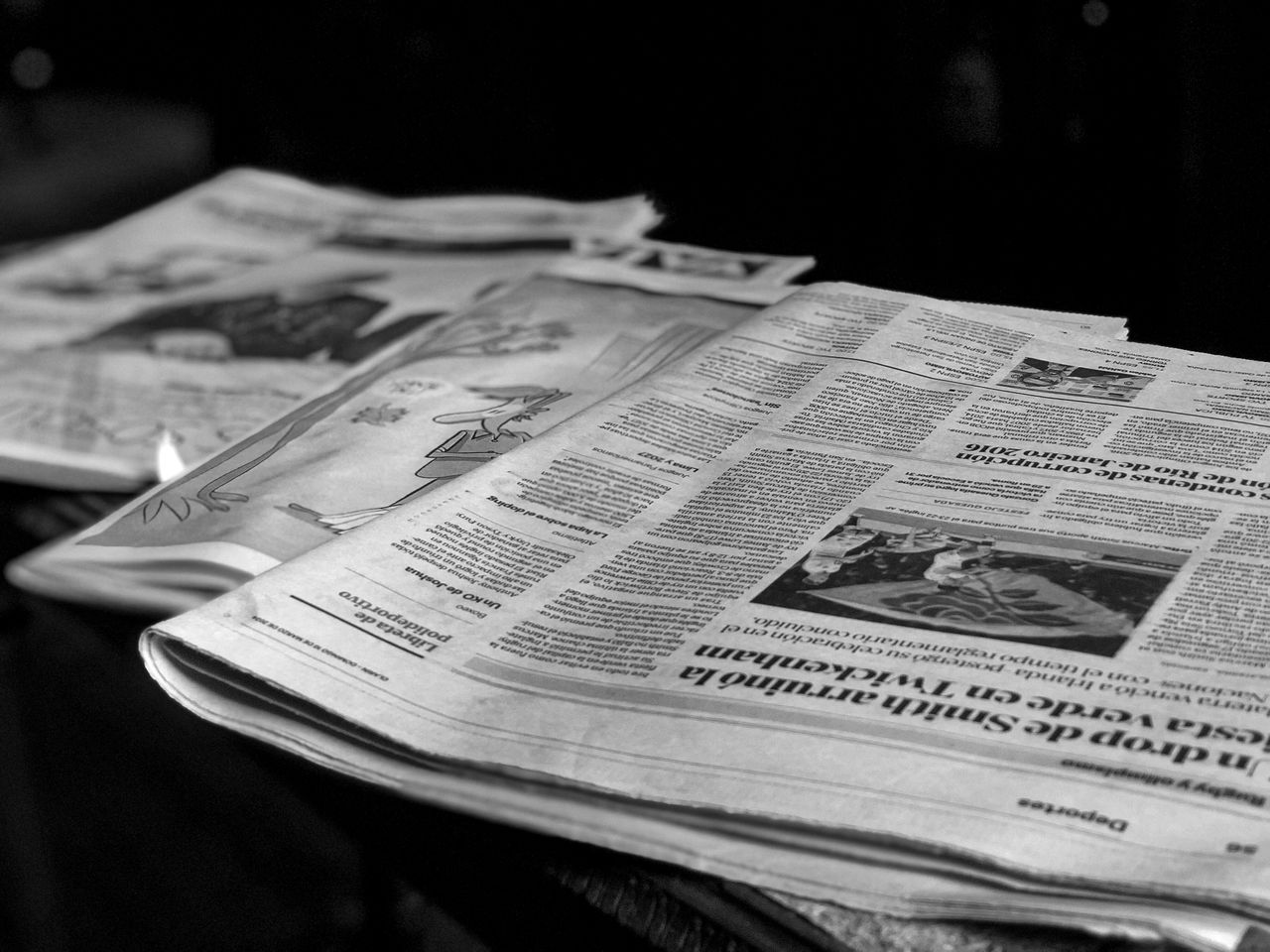 Home Black and white close-up image of newspapers laid on a table, emphasizing print media.