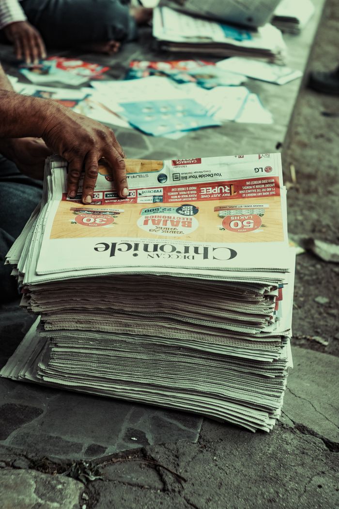 about-img Close-up of a hand sorting newspapers on a pavement, outdoors.
