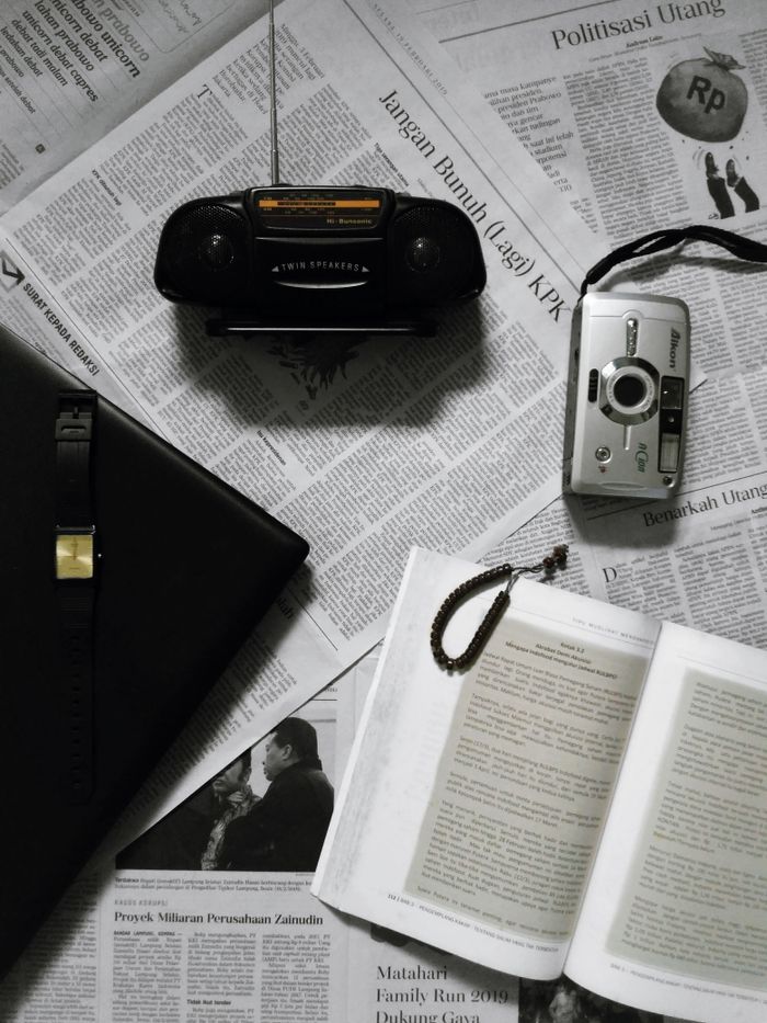A flatlay of vintage camera and gadgets on Indonesian newspapers, featuring books for an artistic touch.