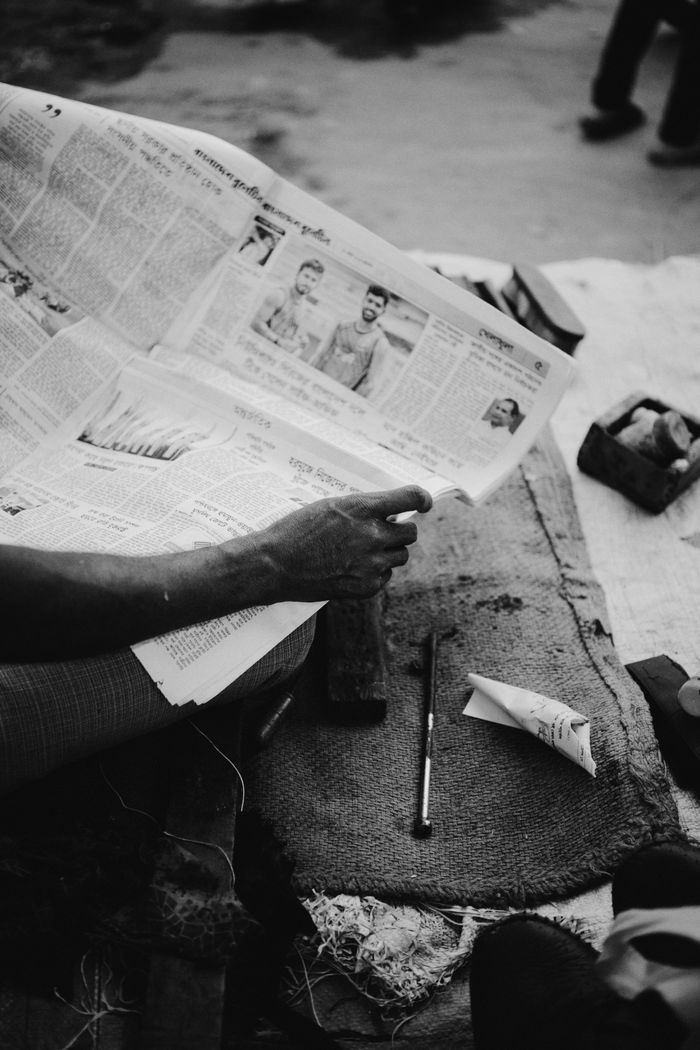 A person reads a newspaper on a street in Kurigram, Bangladesh, capturing daily life in a monochrome style.
