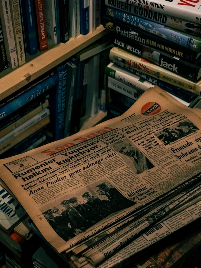 Stack of old newspapers on a bookshelf filled with books in a dark moody ambiance.