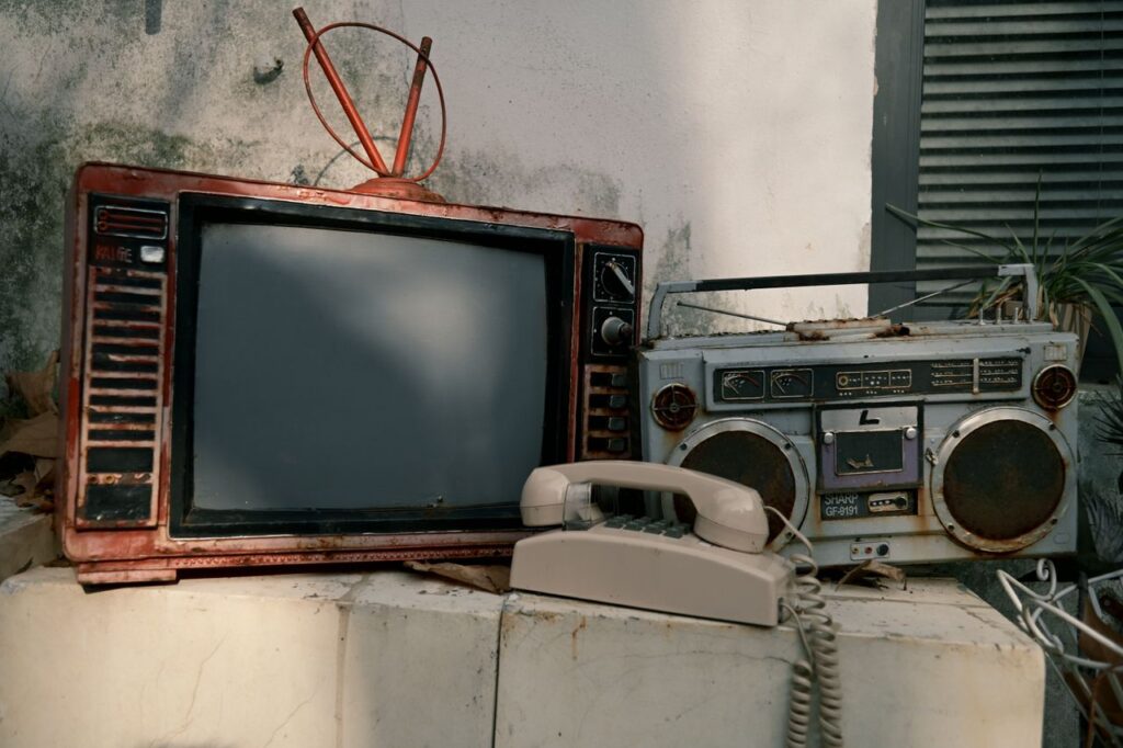 Old TV set, retro radio, and vintage rotary phone in an outdoor setting.
